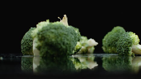 Three-green-fresh-broccoli-fall-on-a-glass-with-splashes-and-drops-of-water-in-slow-motion-on-a-dark-background.-Ingredients-for-Salad-Healthy-Food.